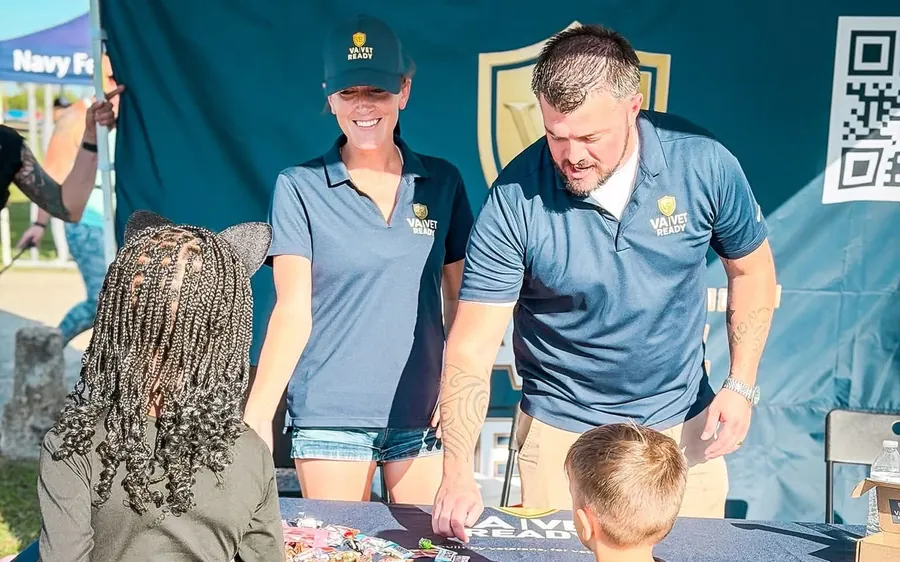 Two VA Ready team members in branded polos handing out candy to two kids in Halloween costumes, a cat and a wizard, at the VA Ready and Vet Ready table during a trick-or-treat event in Copperas Cove, Texas