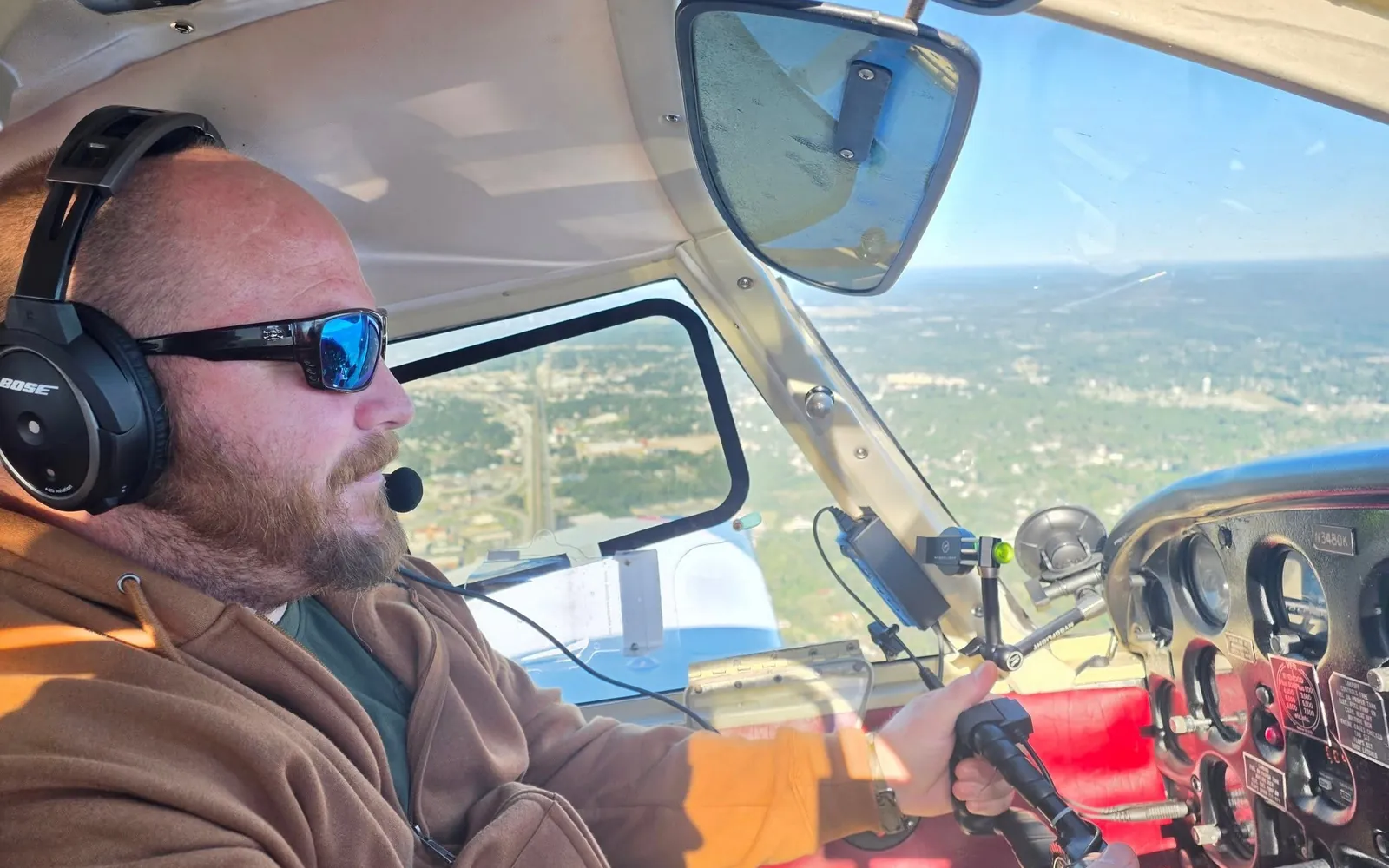 William Tyle, a veteran, at the controls of Piper Cherokee N3480K during a VA Ready sponsored discovery flight, wearing a headset, blue mirrored sunglasses and a brown jacket, with the Georgia landscape below